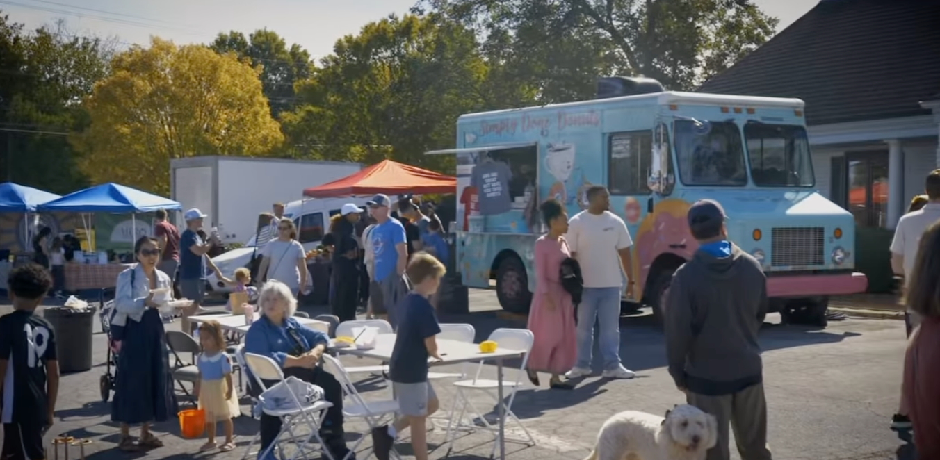 Market visitors gathered around a food truck and tents with tables and seating